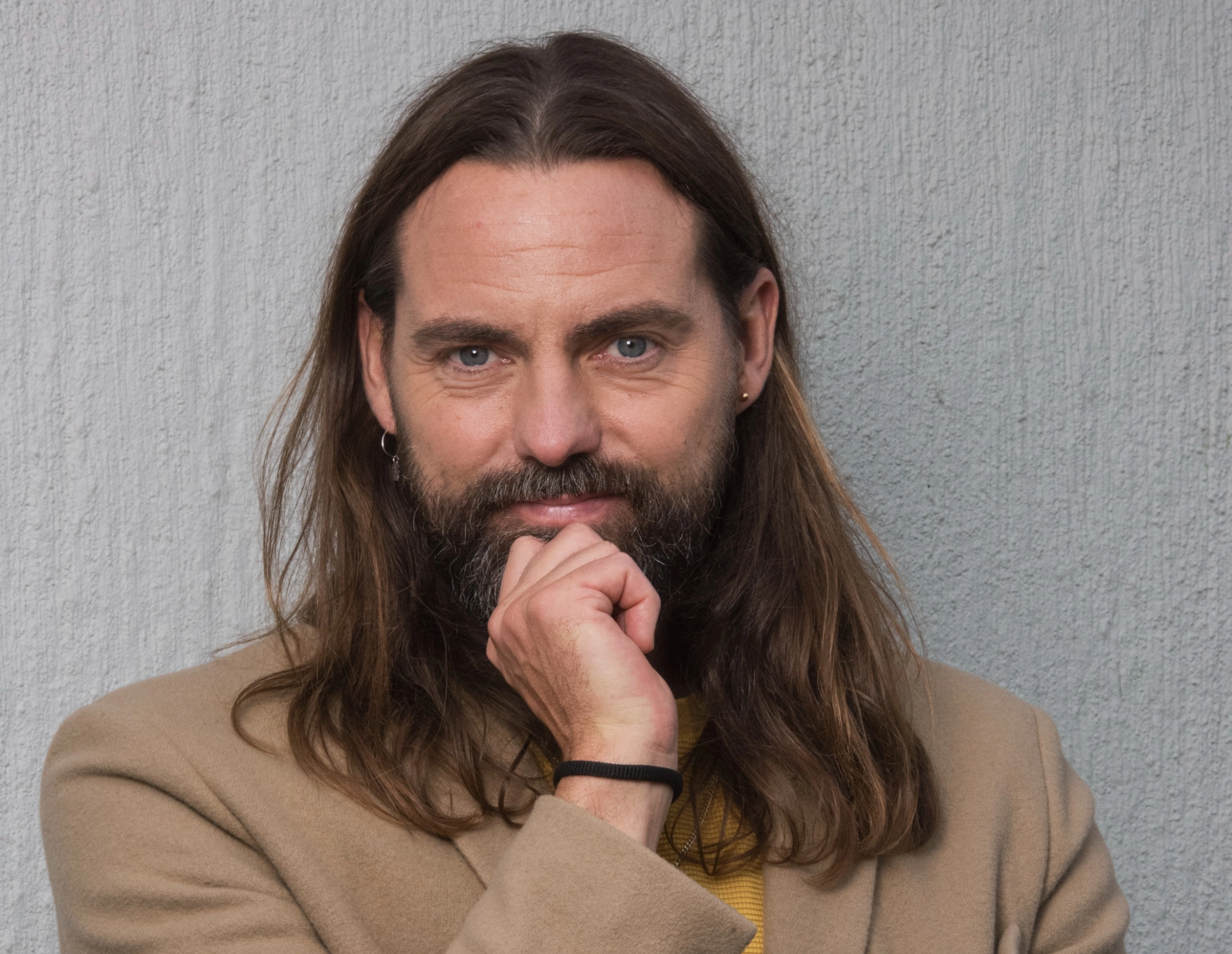 Skribent och  Programledare Nisse Edwall med handen mot hakan i beige kavaj