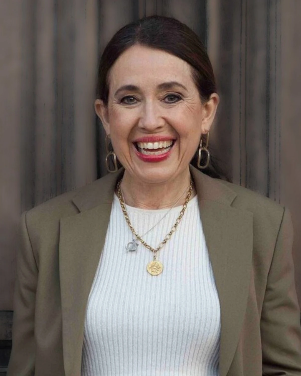 Medieentreprenören Carina Nunstedt leendes med rött läppstift i vit tröja och mörk grön/beige kavaj