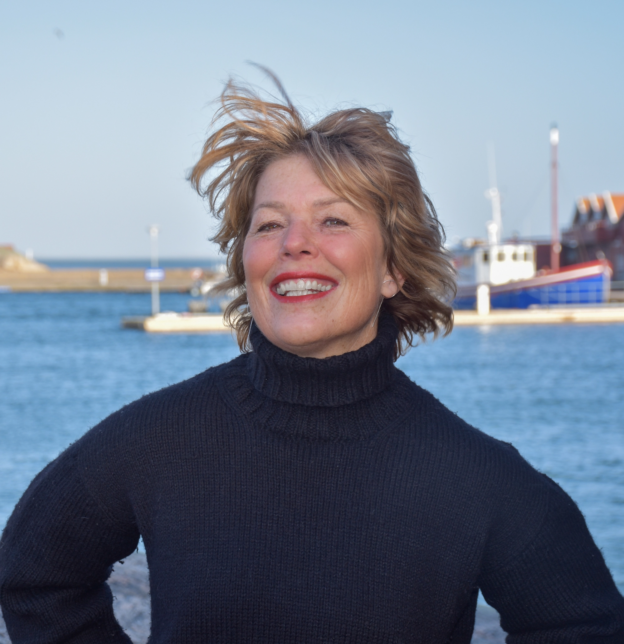 Författaren Malin Lundskog står leende i svart polotröja framför ön Knippla