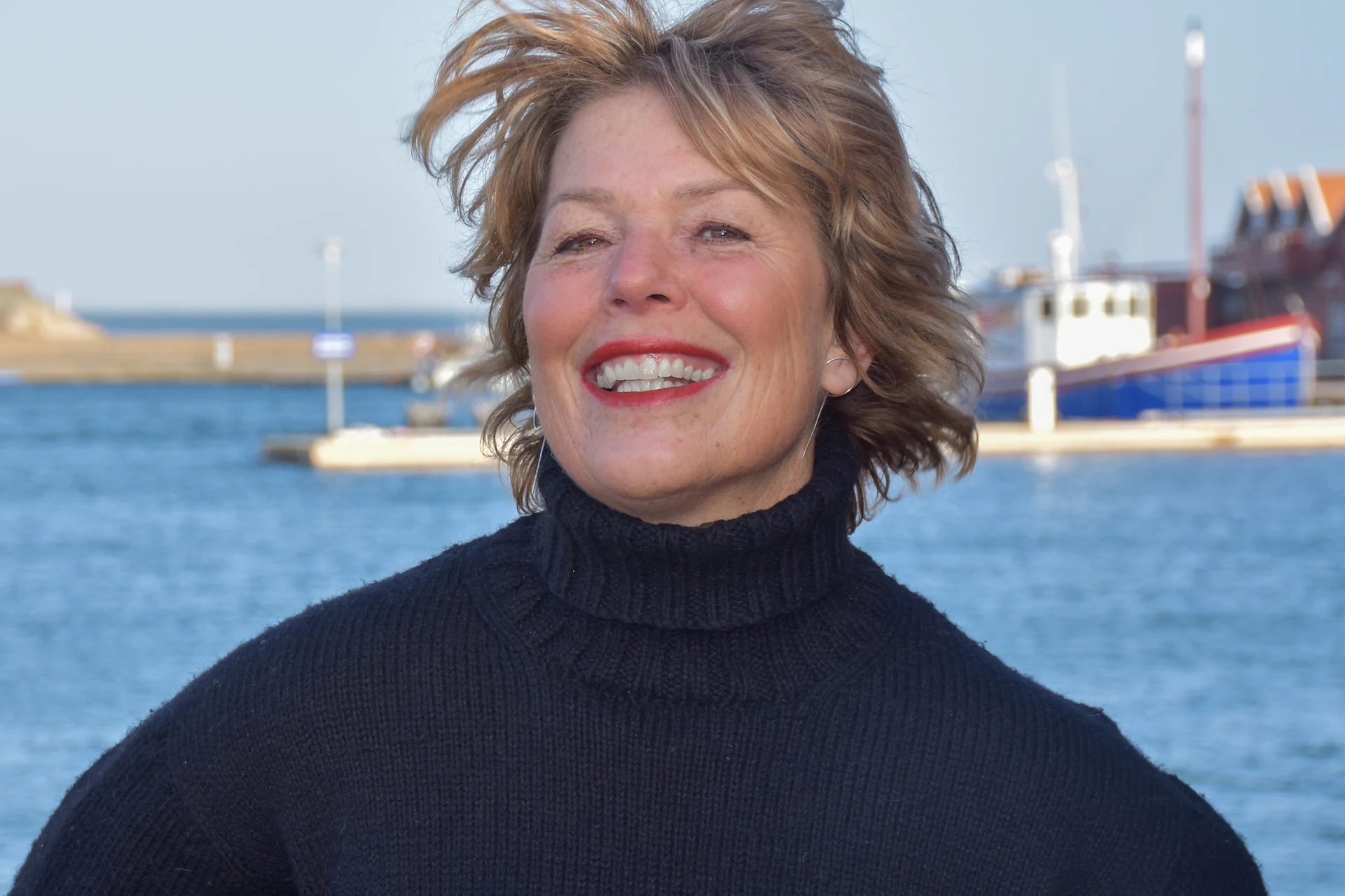 Författaren Malin Lundskog står leende i svart polotröja framför ön Knippla