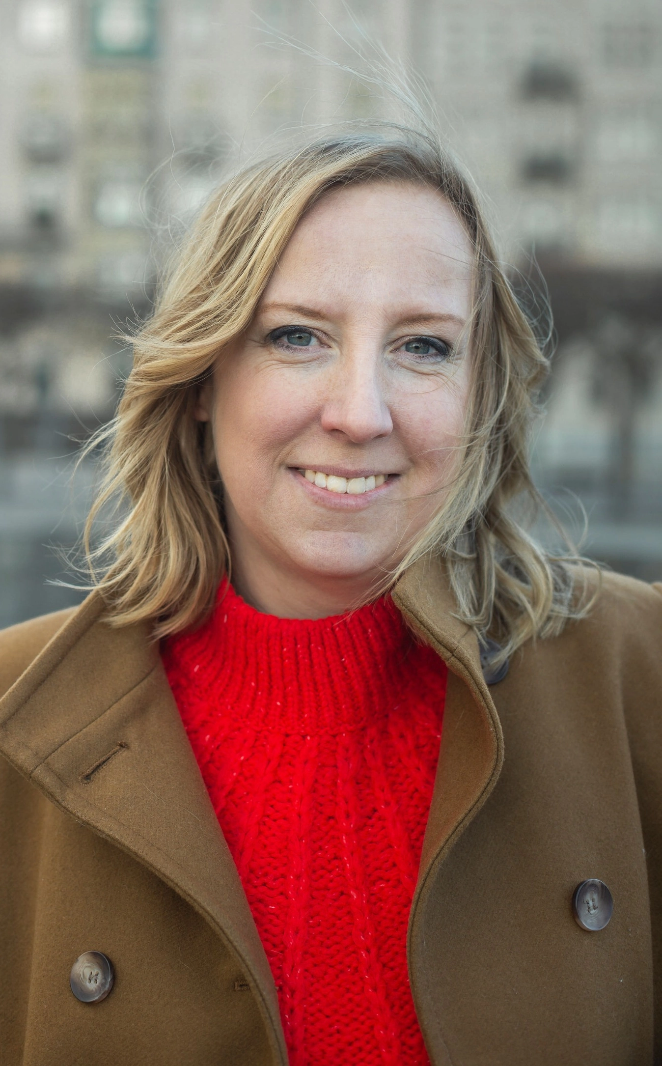 Felicia Welander, Copywriter & Skribent i röd stickad tröja och brun kappa med stan som bakgrund
