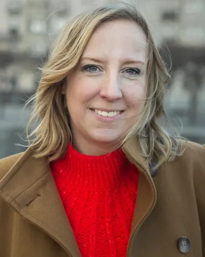 Felicia Welander, Copywriter & Skribent i röd stickad tröja och brun kappa med stan som bakgrund