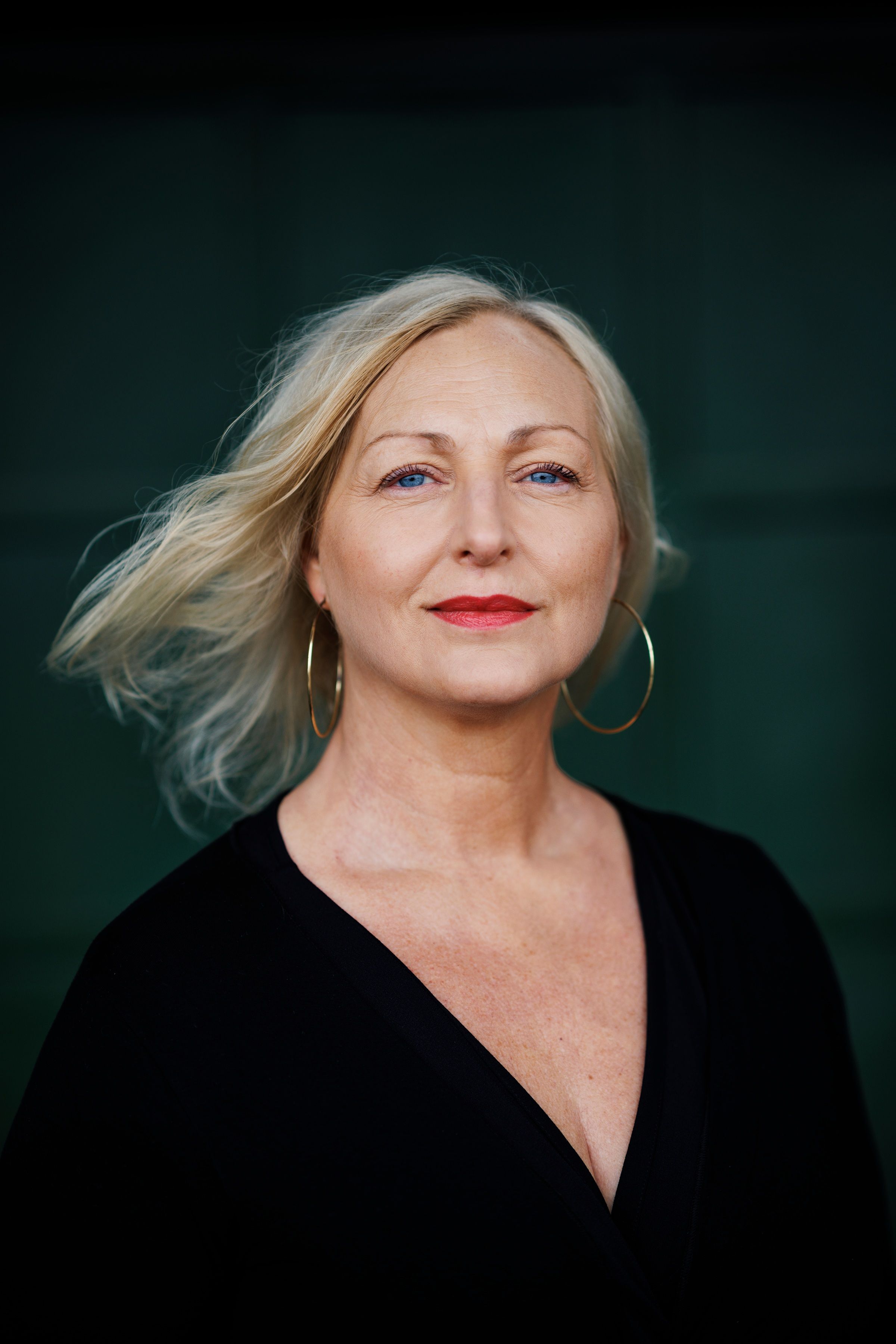 Författaren Lois Steen ser in i kameran med beslutsam blick och styrka. Hon är klädd i svart, har rött läppstift och stora örhängen.