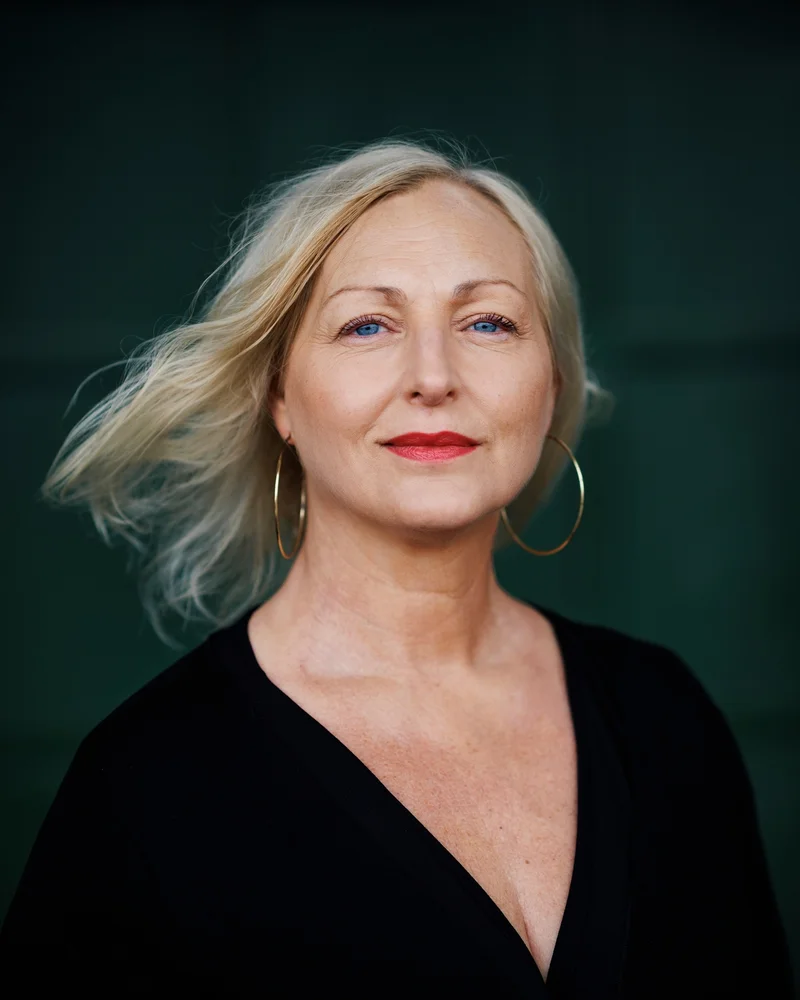 Författaren Lois Steen ser in i kameran med beslutsam blick och styrka. Hon är klädd i svart, har rött läppstift och stora örhängen.