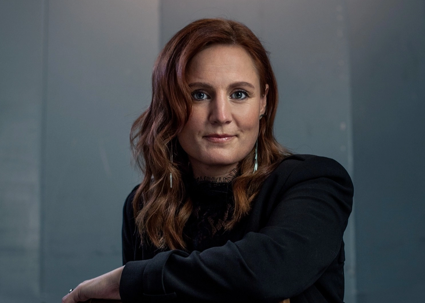 Häftigt porträttfoto av poddaren och föreläsaren Anna Bågenstam i mörk tröja sittandes över en stol