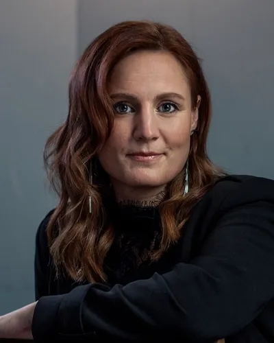 Häftigt porträttfoto av poddaren och föreläsaren Anna Bågenstam i mörk tröja sittandes över en stol