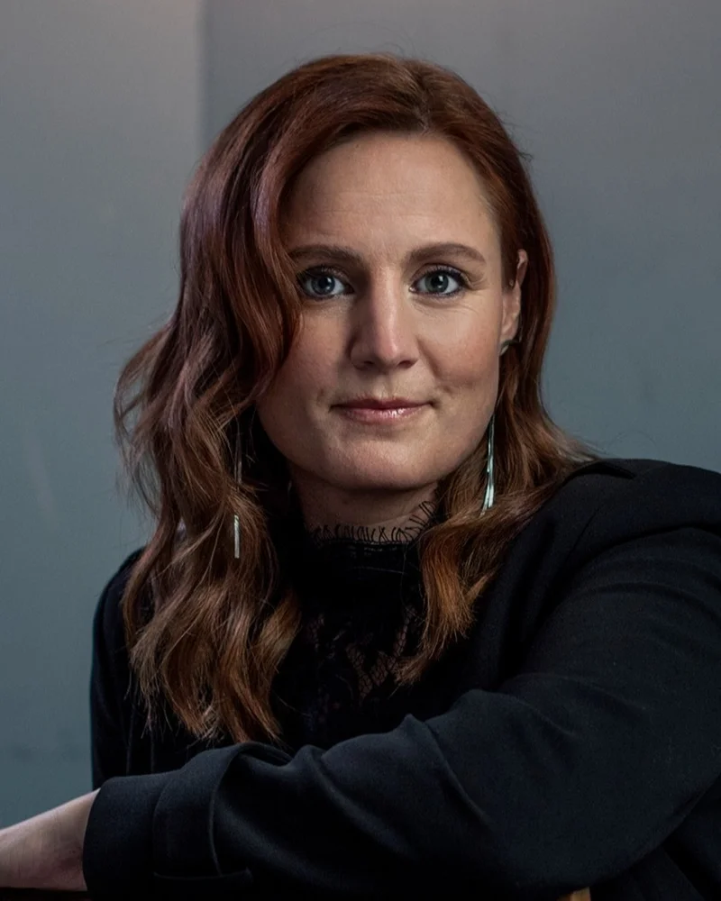 Häftigt porträttfoto av poddaren och föreläsaren Anna Bågenstam i mörk tröja sittandes över en stol