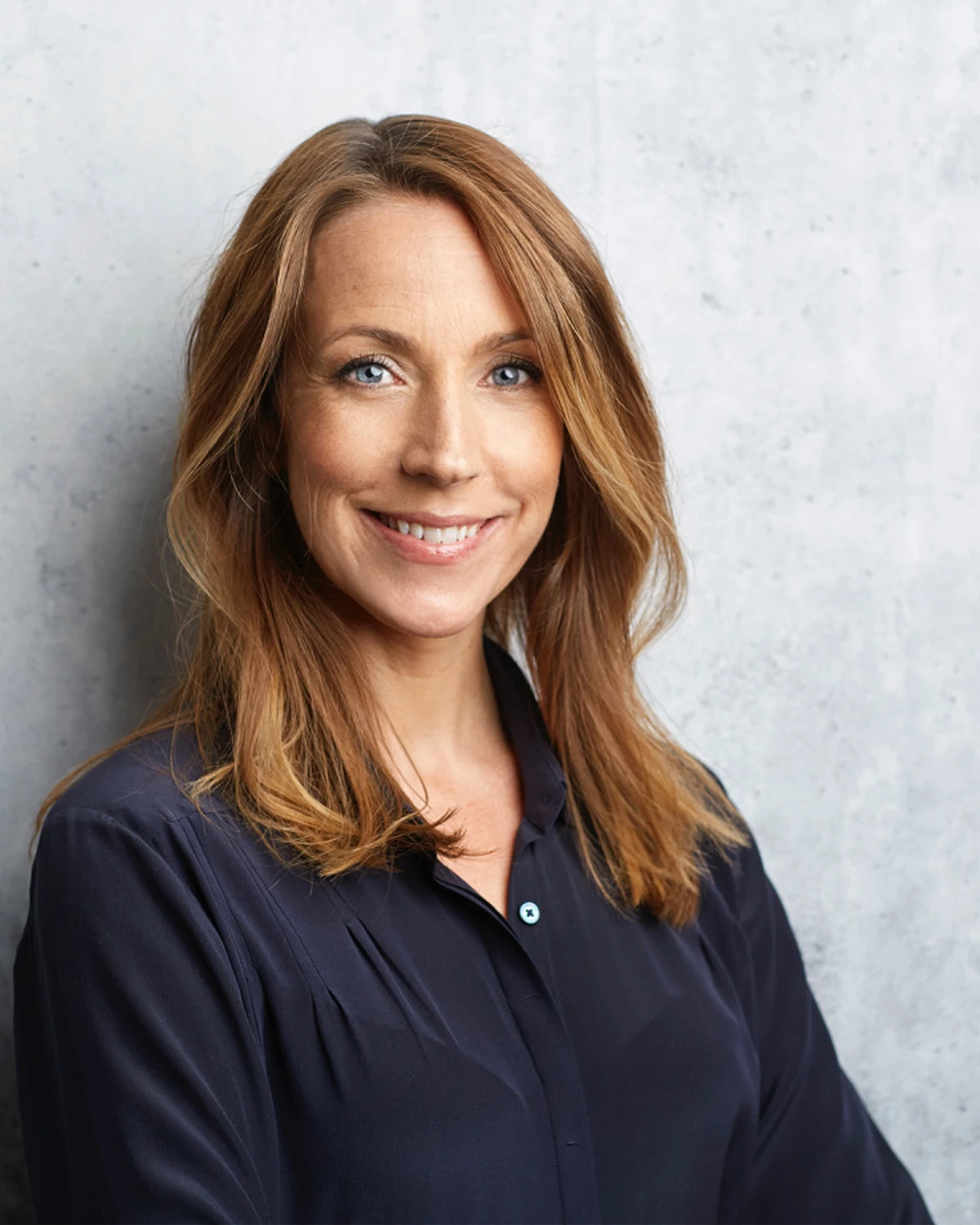 Bilden visar psykologen och författaren Anna Bennich, stående mot en ljusgrå vägg, leende i en blå blus.