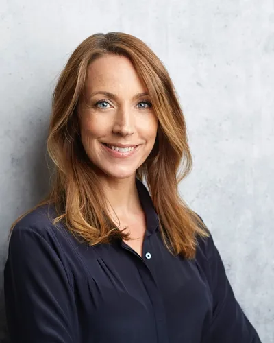 Bilden visar psykologen och författaren Anna Bennich, stående mot en ljusgrå vägg, leende i en blå blus.