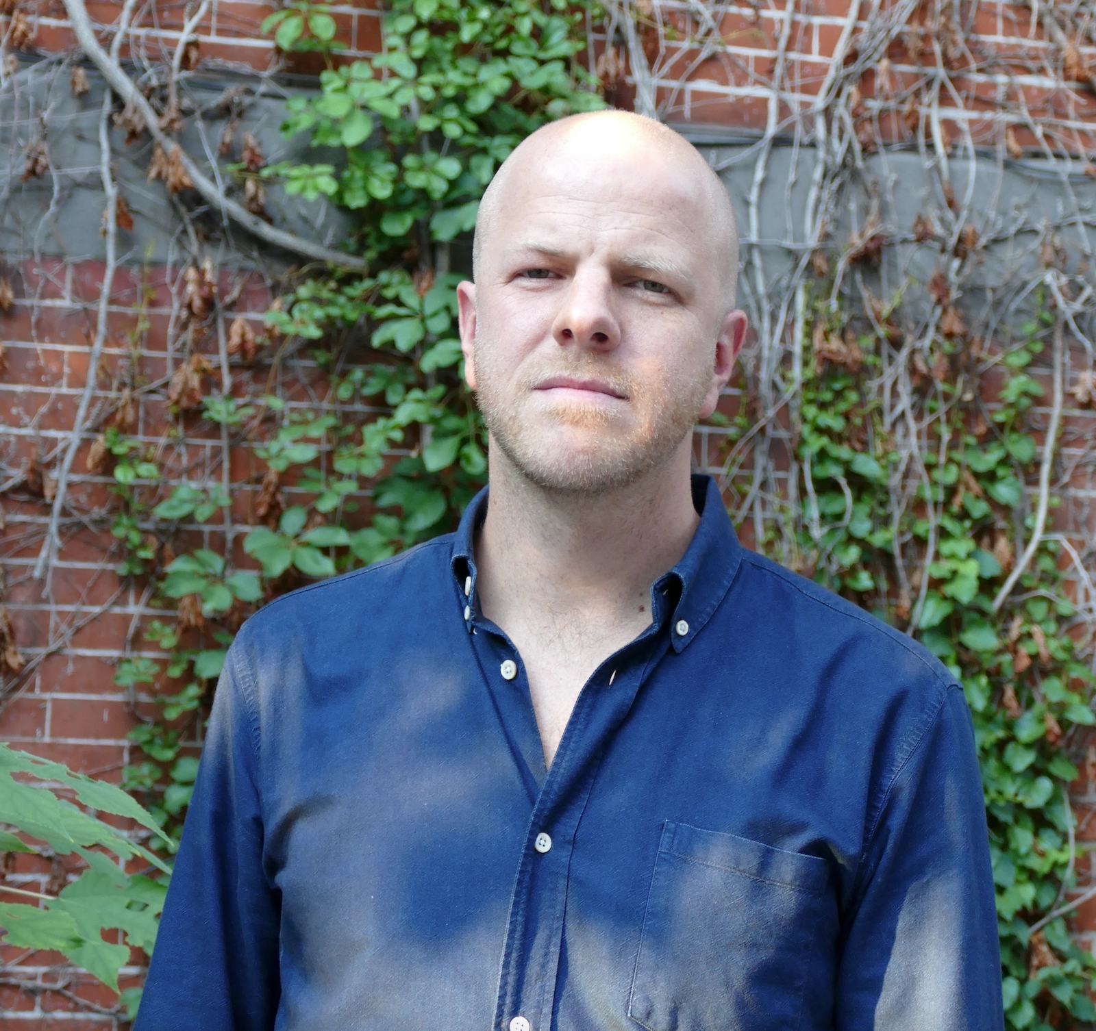 Bilden visar journalisten Martin Gelin klädd i blå skjorta framför en tegelvägg. 