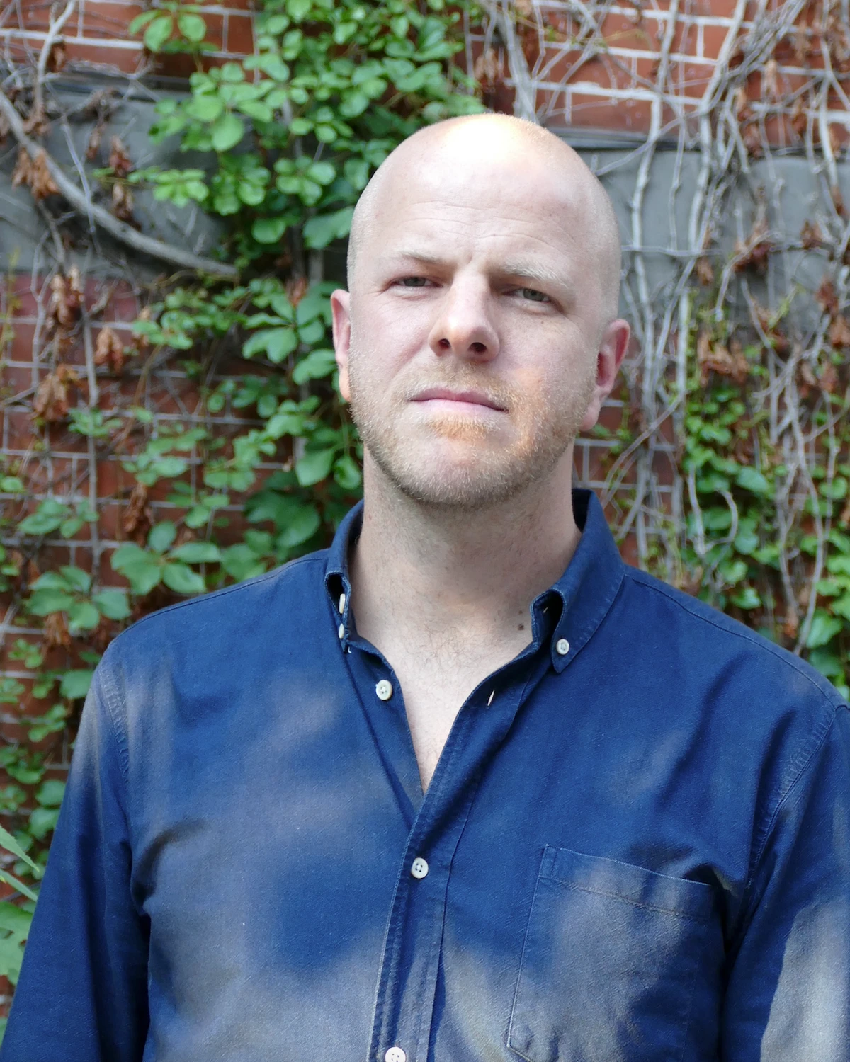 Bilden visar journalisten Martin Gelin klädd i blå skjorta framför en tegelvägg.