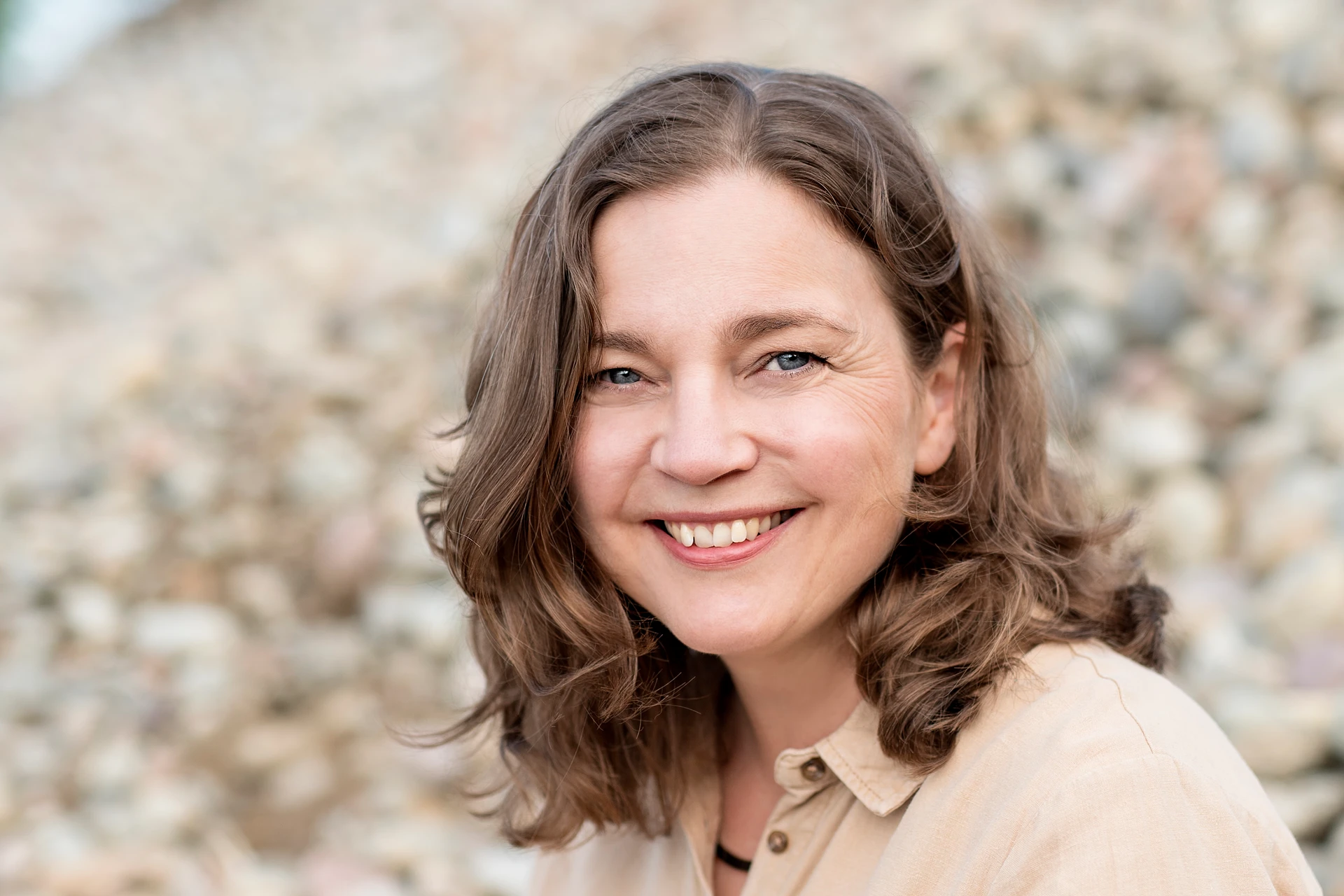 Porträtt av Lena Zetterberg Björk, copywriter och kursledare, i beige skjorta med ljusbrun stenstrand i bakgrunden.