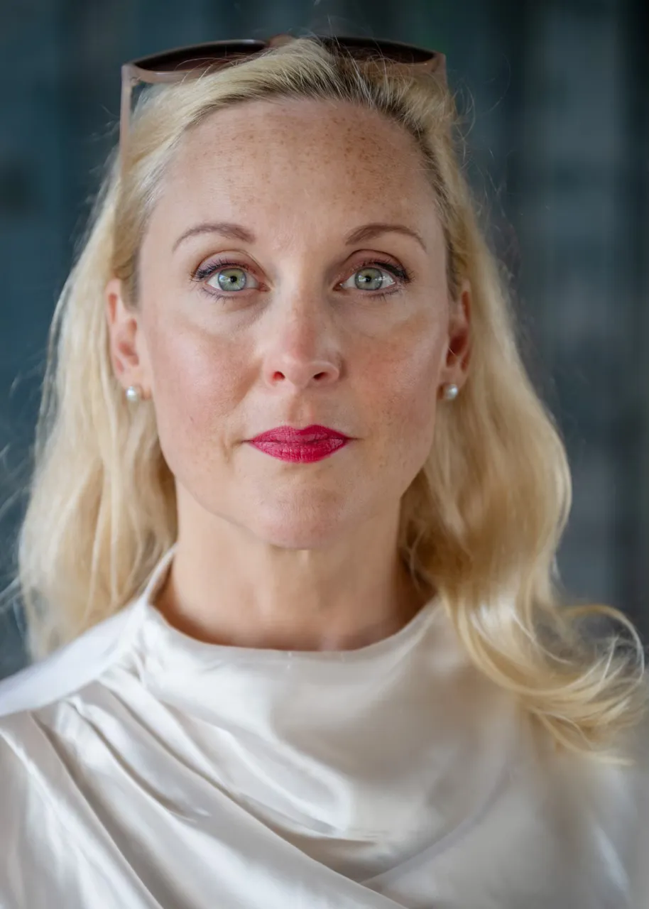 Författaren Lisa Bjurwald ser in i kameran. Hon bär rött läppstift och har solglasögonen i håret.