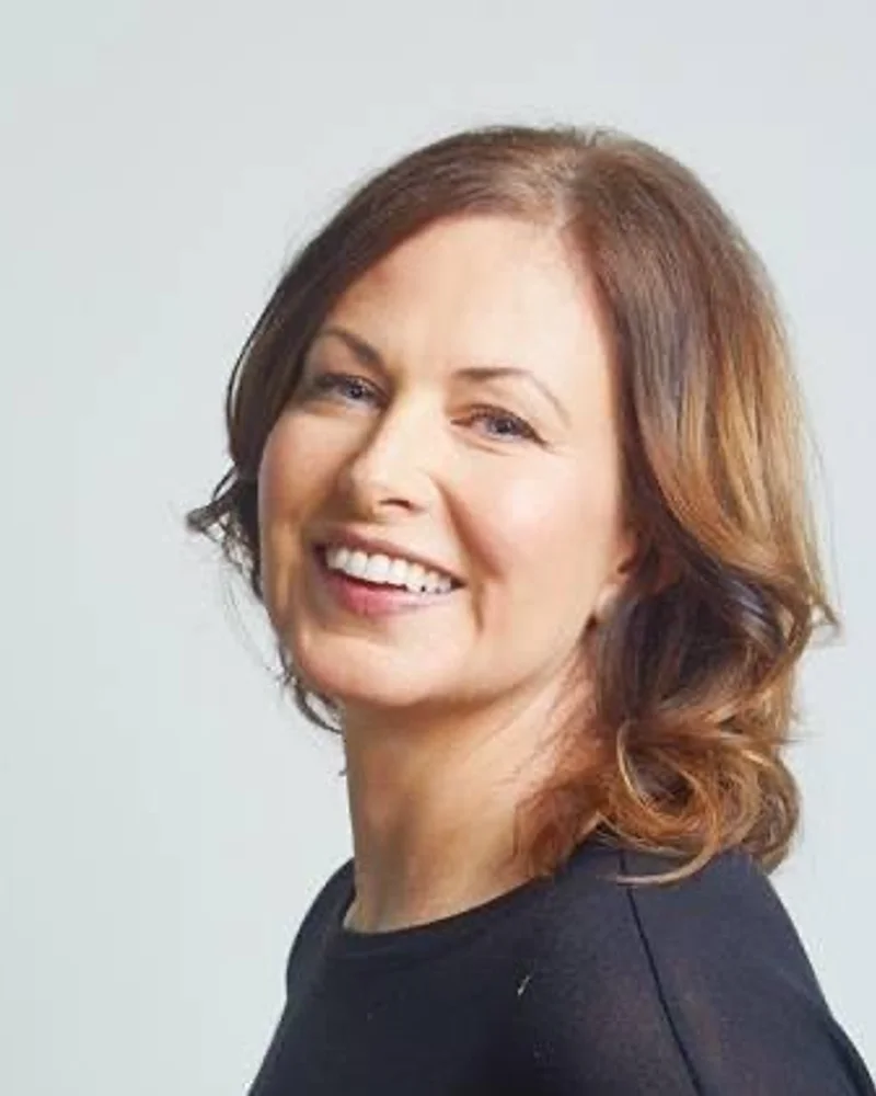 En mörkhårig kvinna ler in i kameran.