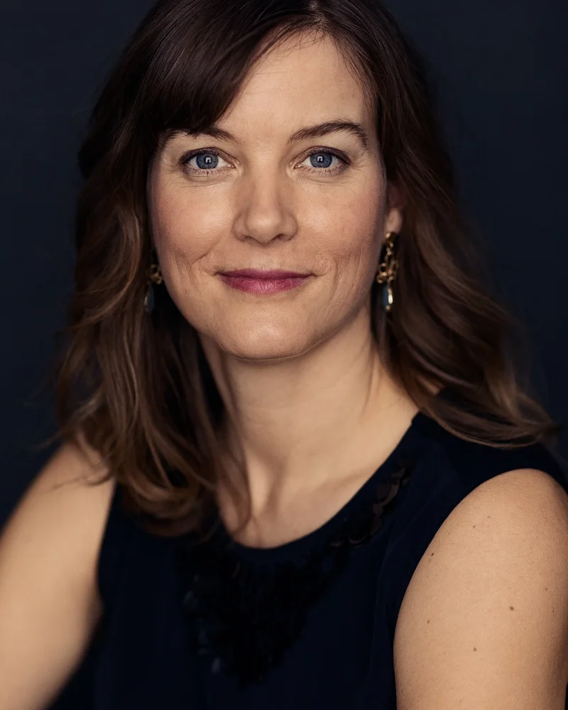 En mörkhårig kvinna klädd i svart linne blickar in i kameran med ett leende.