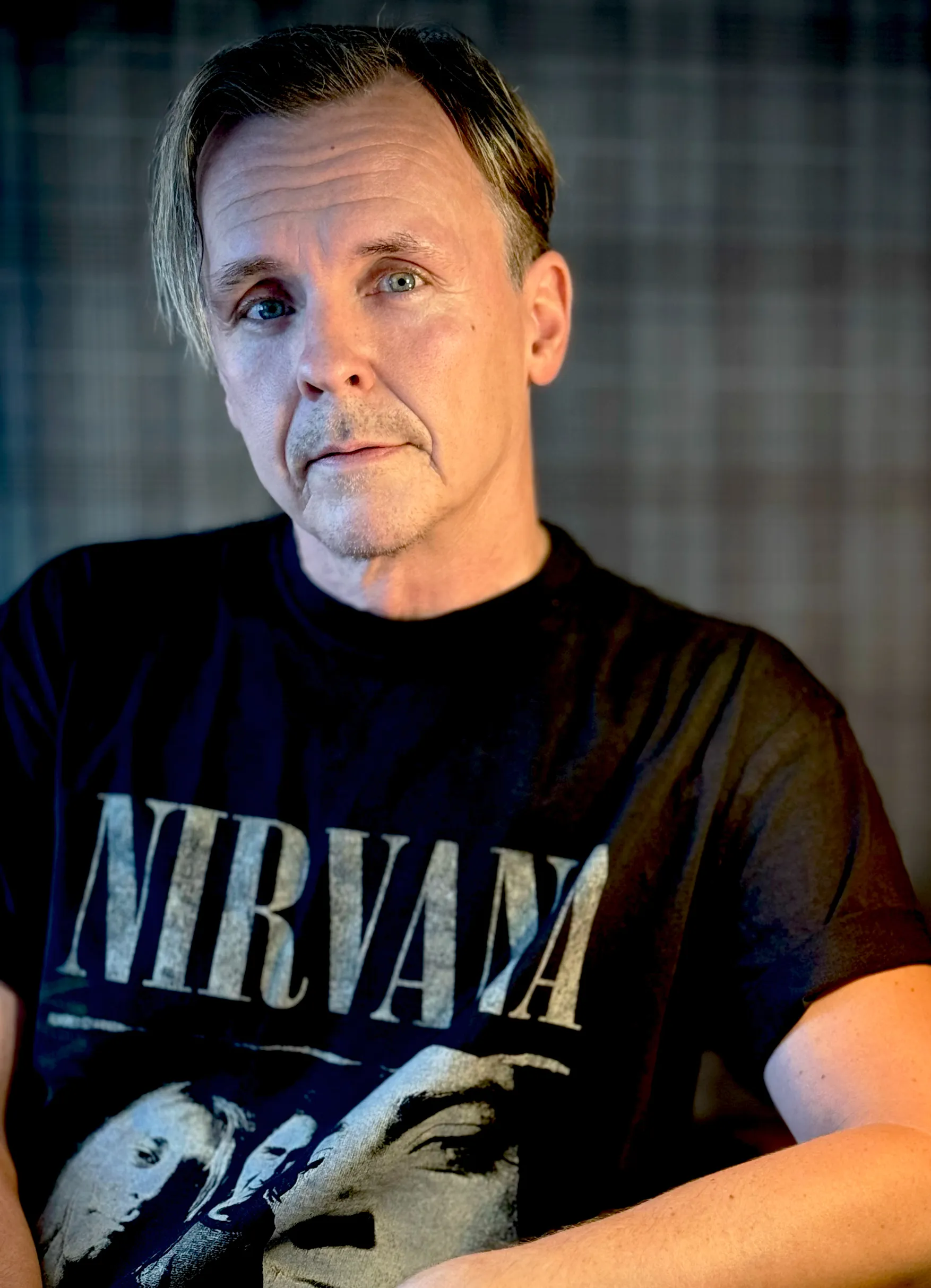 Porträttfoto av Mikael Newihl i svart Nirvana t-shirt mot grårutig bakgrund