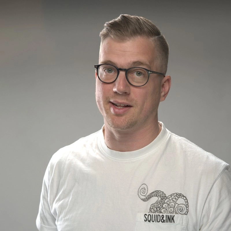Porträttfoto av den digitala taktikerna Jesper Åström i vit t-shirt mot grå bakgrund