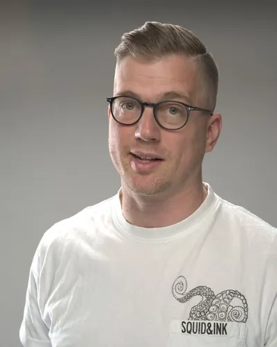 Porträttfoto av den digitala taktikerna Jesper Åström i vit t-shirt mot grå bakgrund