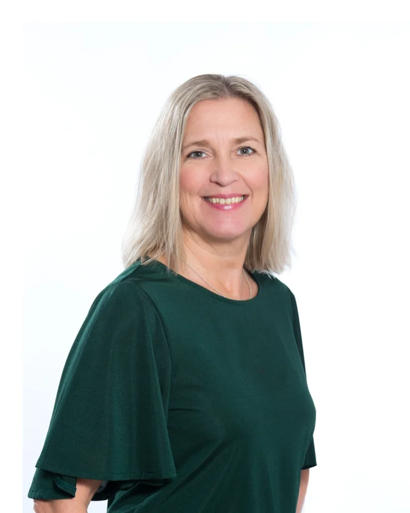 En kvinna i blont hår och grön tröja ler in i kameran.