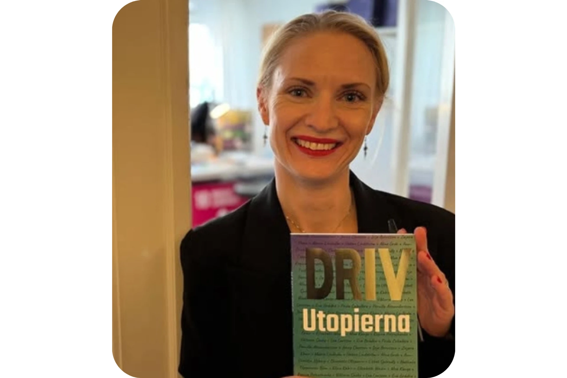 Elisabeth Wadin står i en dörröppning, ler och håller boken Driv Utopierna i handen.