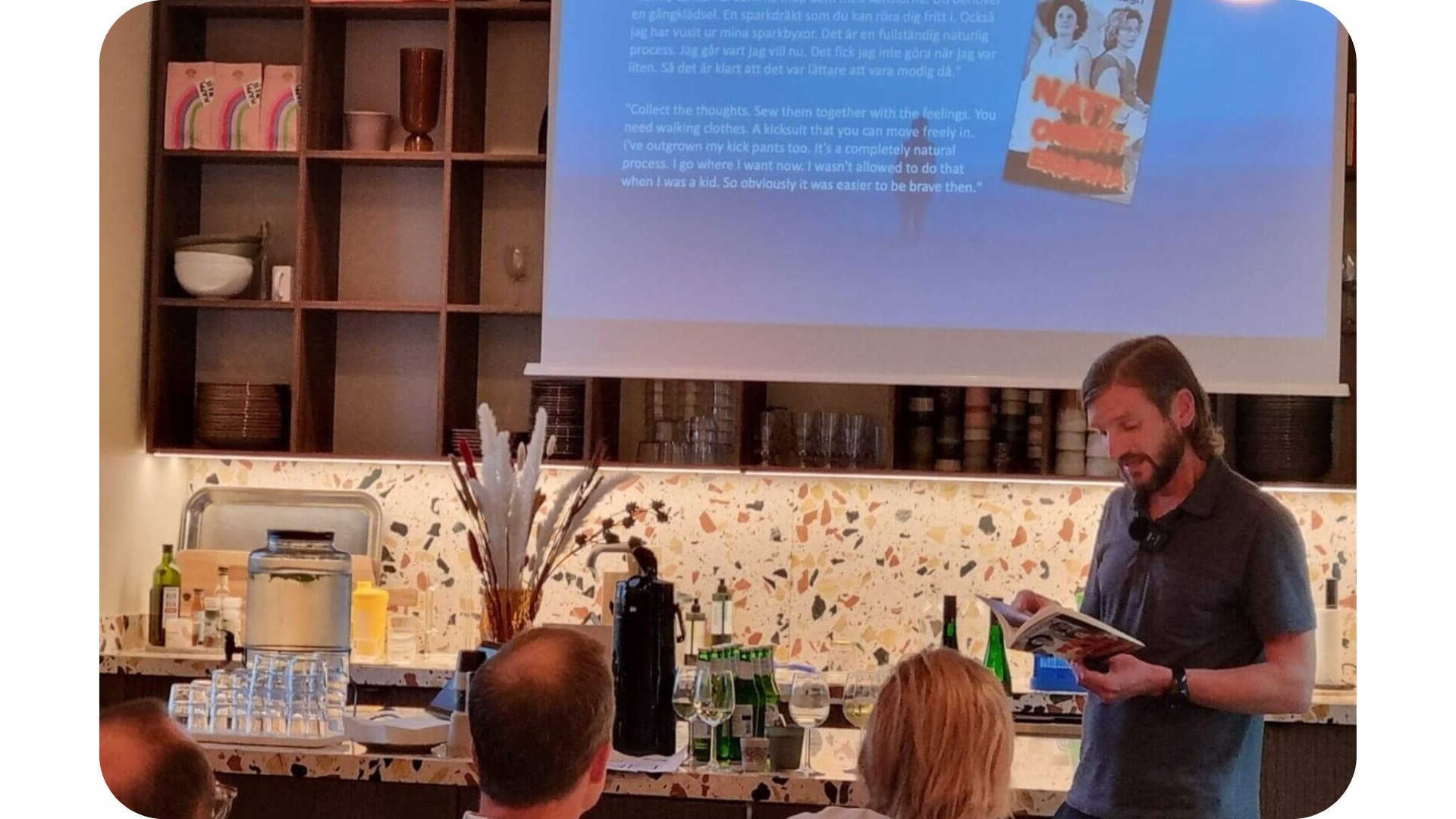 Klas Fjärstedt föreläser i en aula framför publik och håller i en bok, åhörarna sitter framför honom.