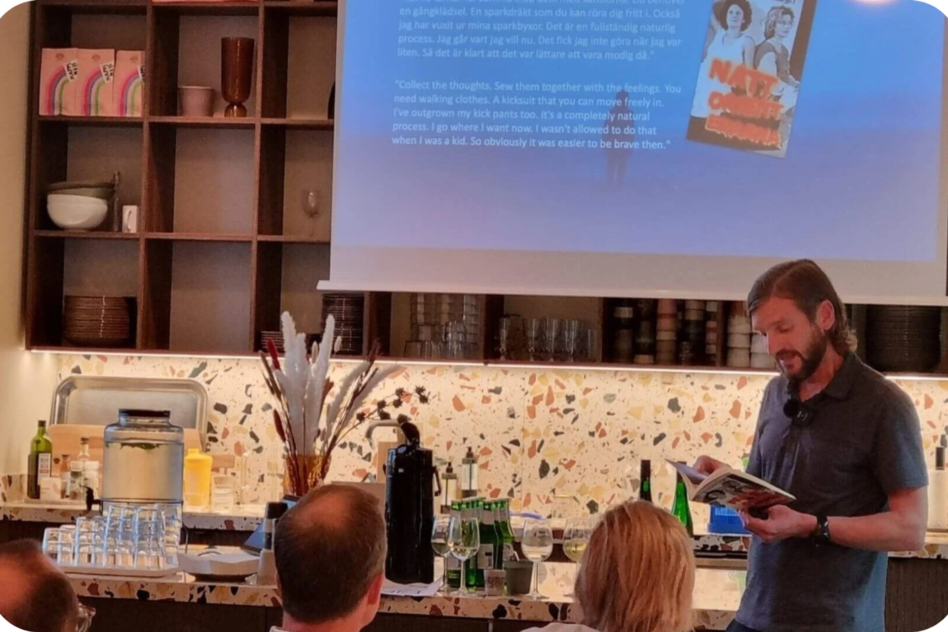 Klas Fjärstedt föreläser i en aula framför publik och håller i en bok, åhörarna sitter framför honom.