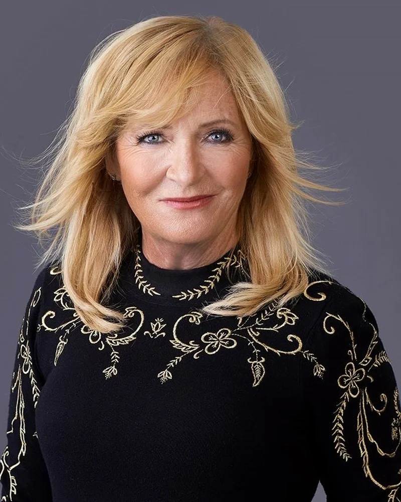 Journalist, Programledare & Författare Malou von Sivers i mörk tröja med gulddetaljer, vind i håret leendes mot kameran