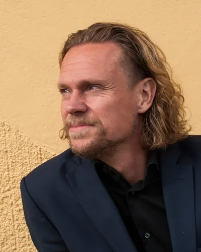 Christer Pettersson i mörkblå kavaj mot mjukgul vägg