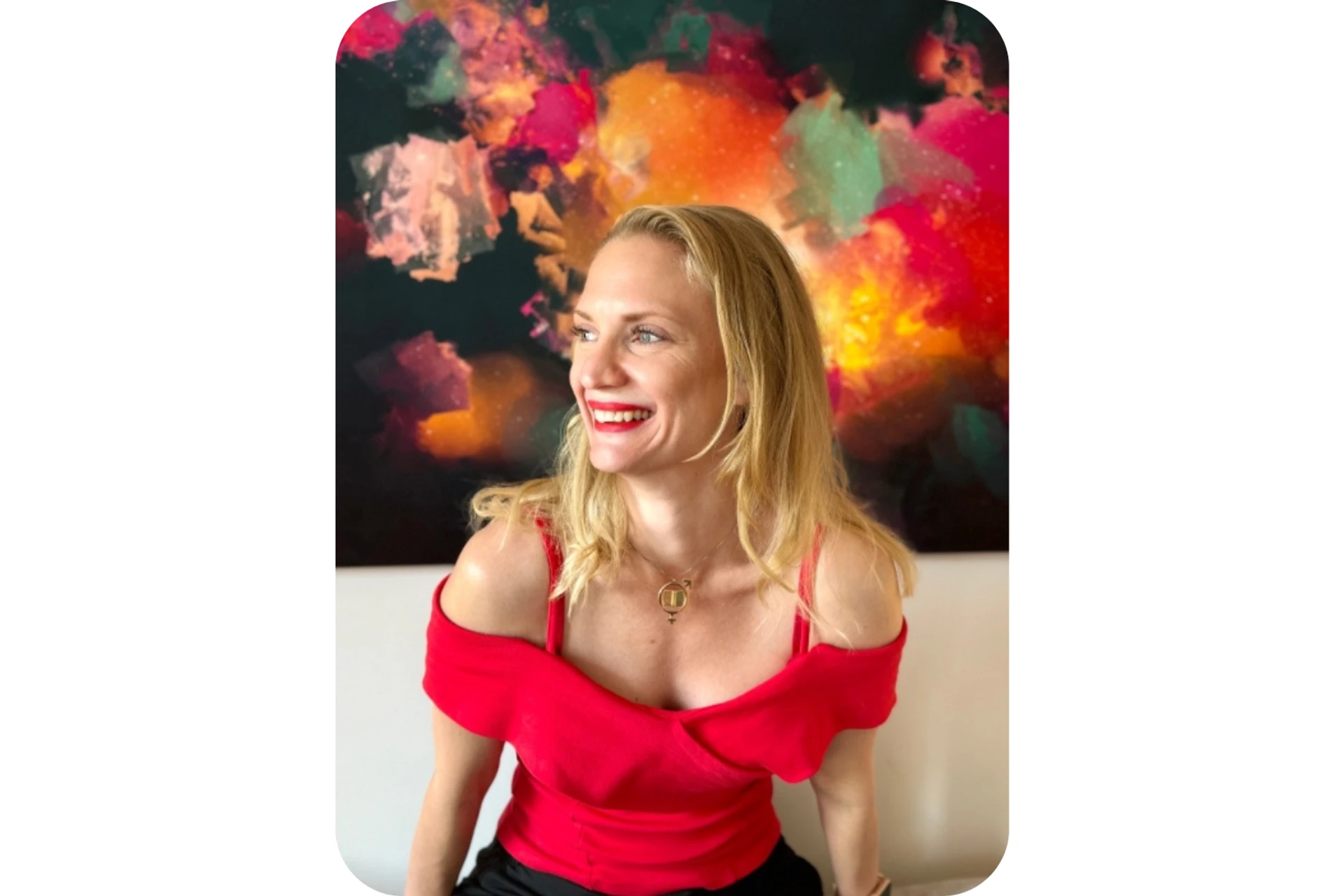 Elisabeth Wadin med ljust hår sitter i en soffa och ler, tittande åt sidan. Hon bär en röd topp och bakom henne hänger en färgglad tavla.