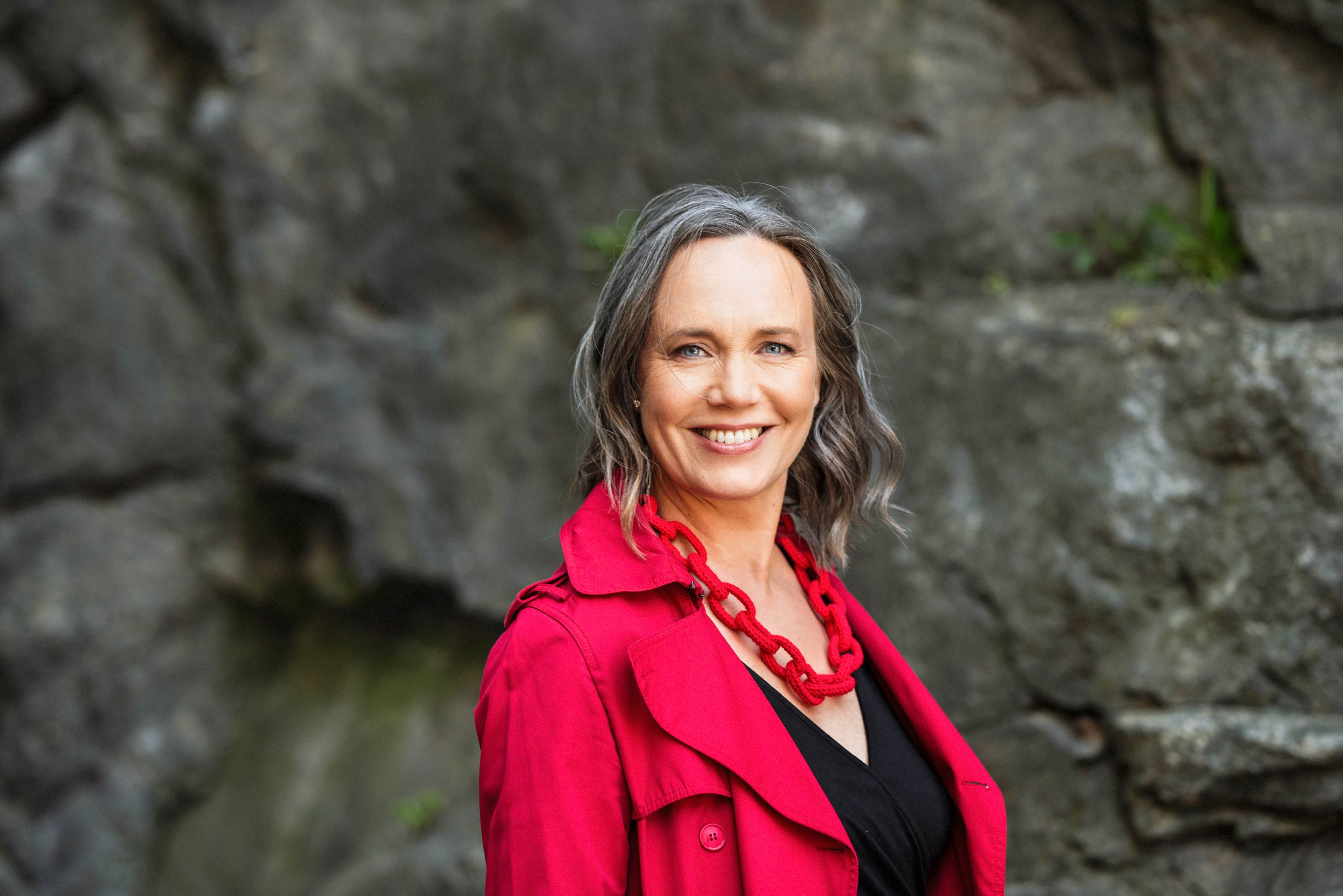 Psykologen och föreläsaren Maria Farm står leende i lysande röd kappa och ett rött halsband.