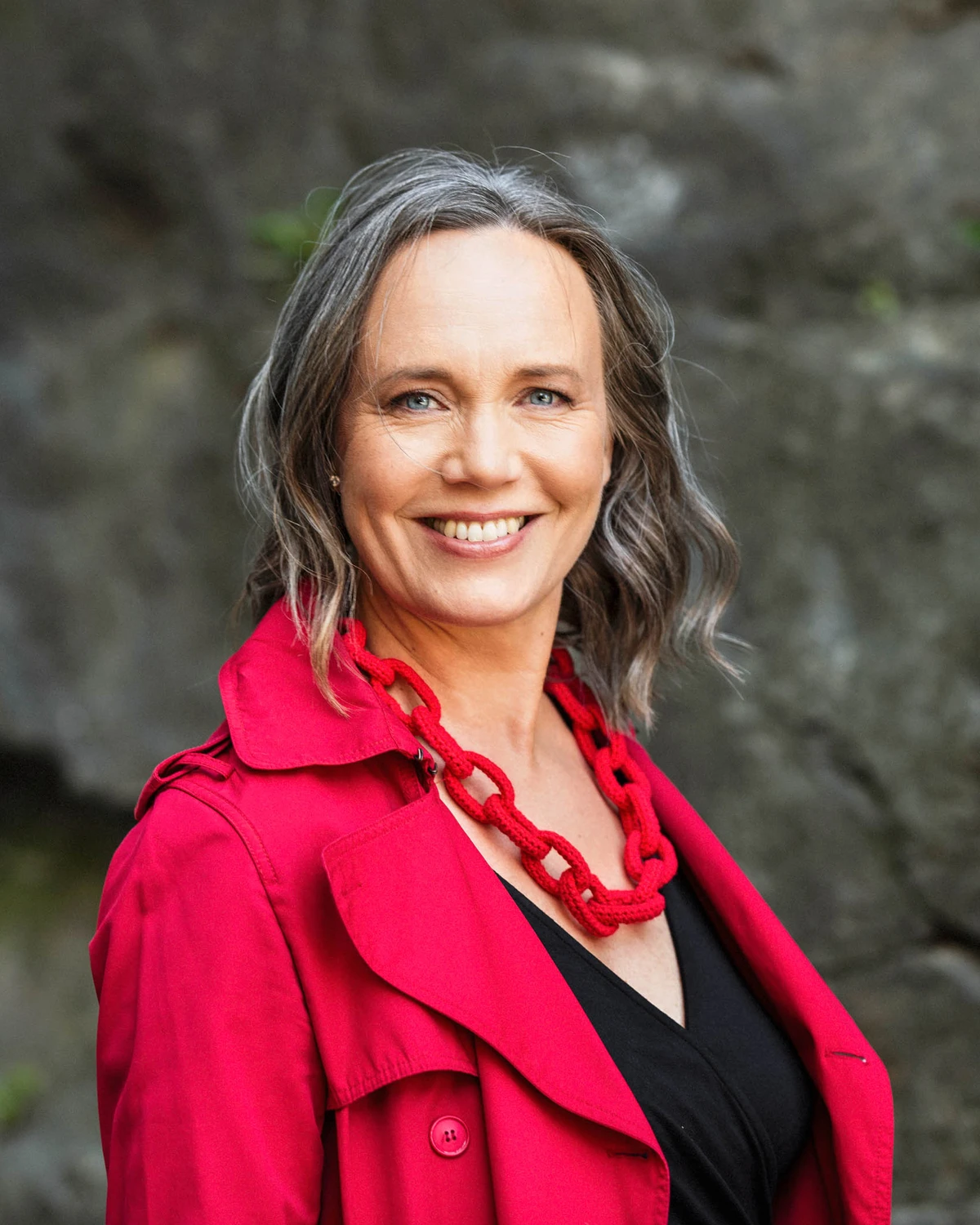 Psykologen och föreläsaren Maria Farm står leende i lysande röd kappa och ett rött halsband.