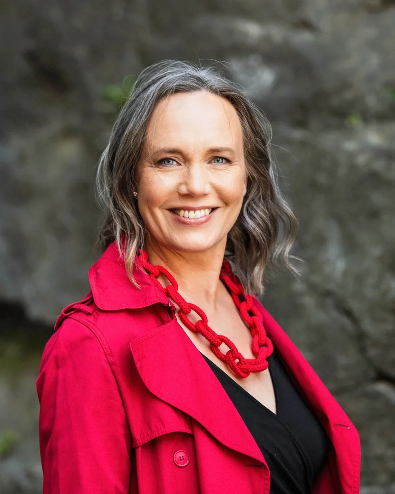 Psykologen och föreläsaren Maria Farm står leende i lysande röd kappa och ett rött halsband.