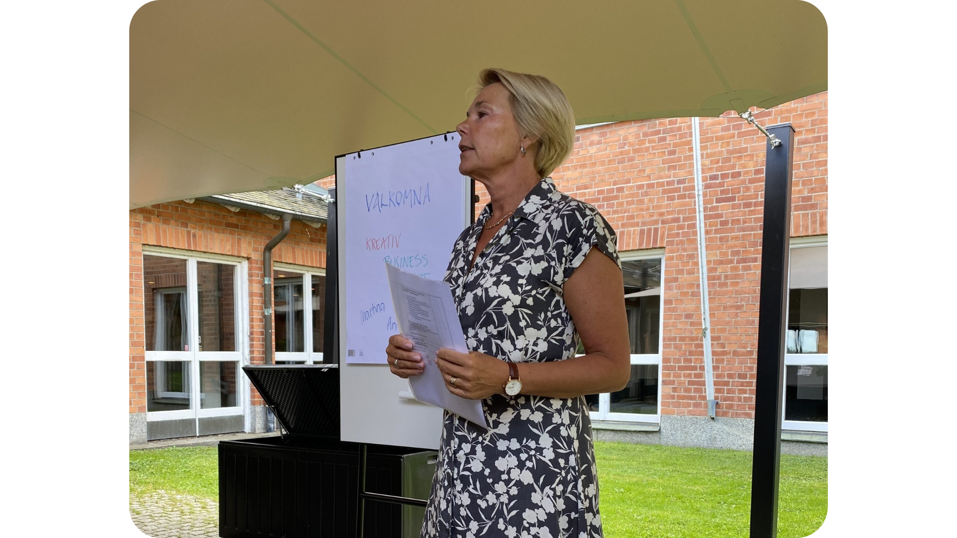 Martina Brandt står med papper i handen och talar, bakom henne syns en whiteboard och stora glaspartier mot utmohusmiljö.