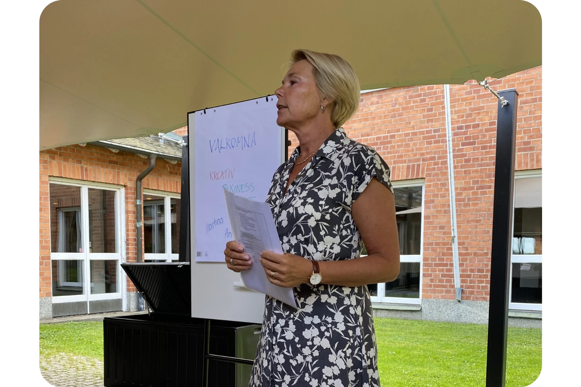 Martina Brandt står med papper i handen och talar, bakom henne syns en whiteboard och stora glaspartier mot utmohusmiljö.