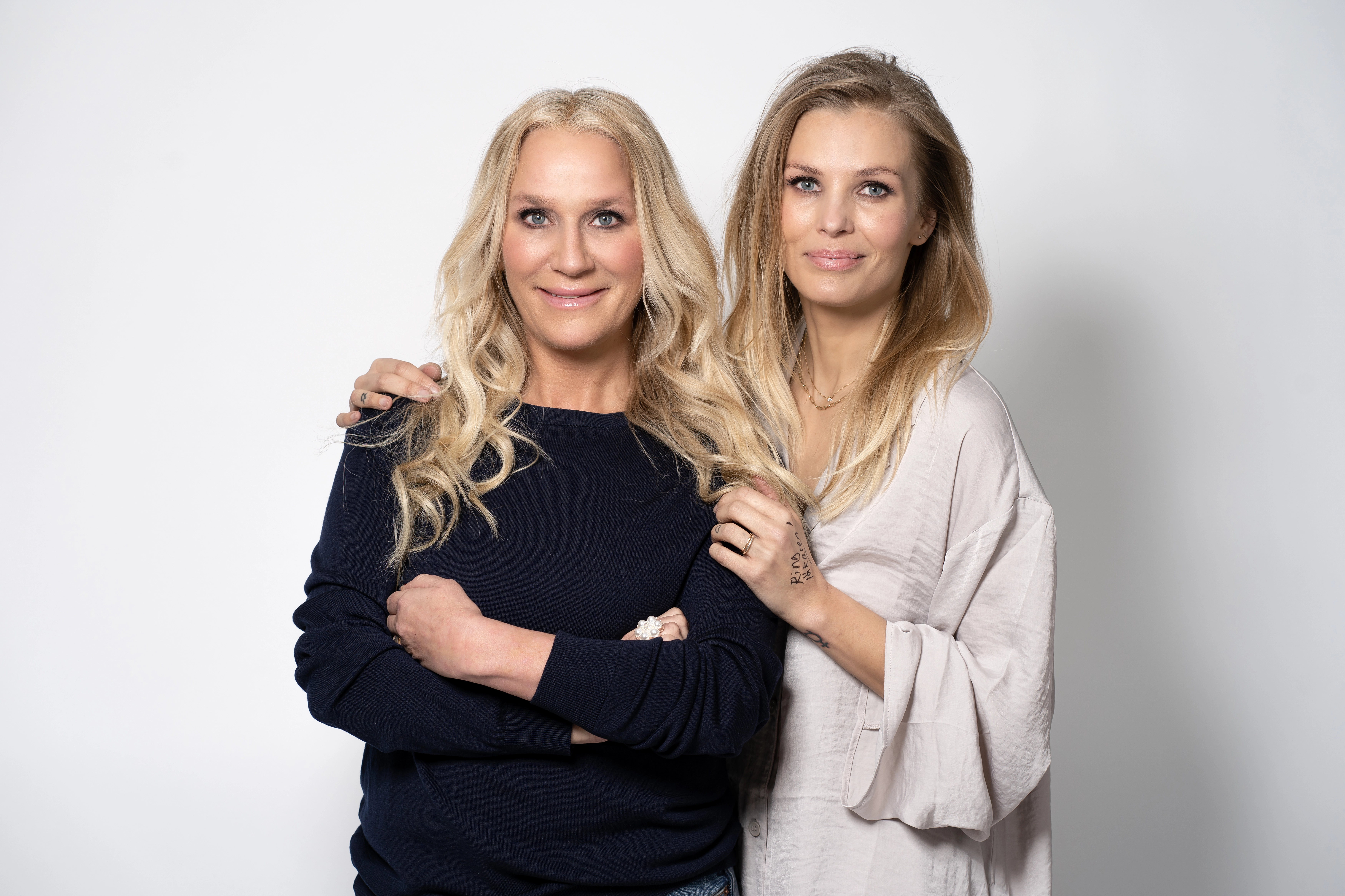 Stjärnduon Ann Söderlund och Fi Lindfors står tätt tillammans och tittar leende in i kameran. 