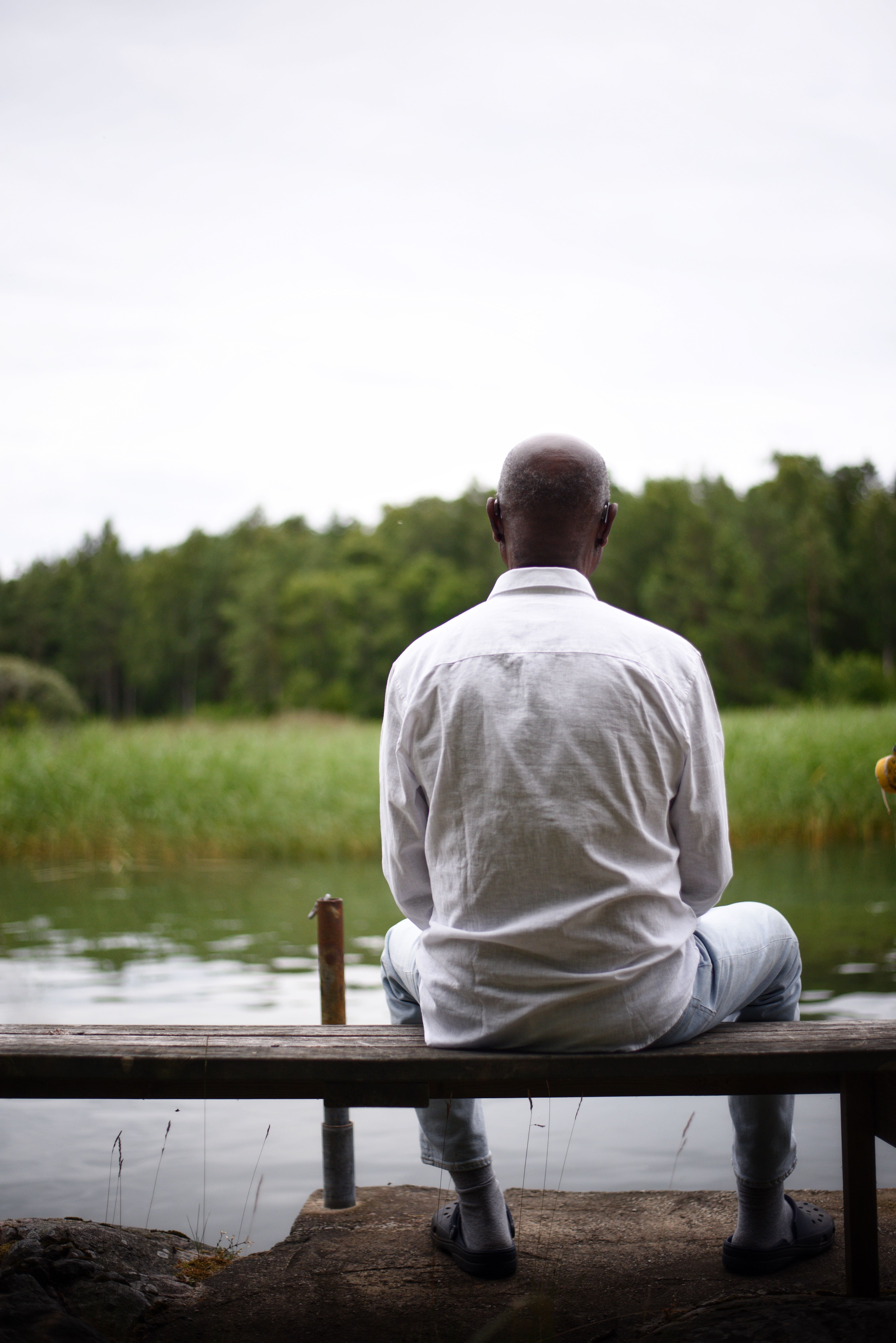 Amadou Jallow sitter på en liten brygga och ser ut över skog och sjö.