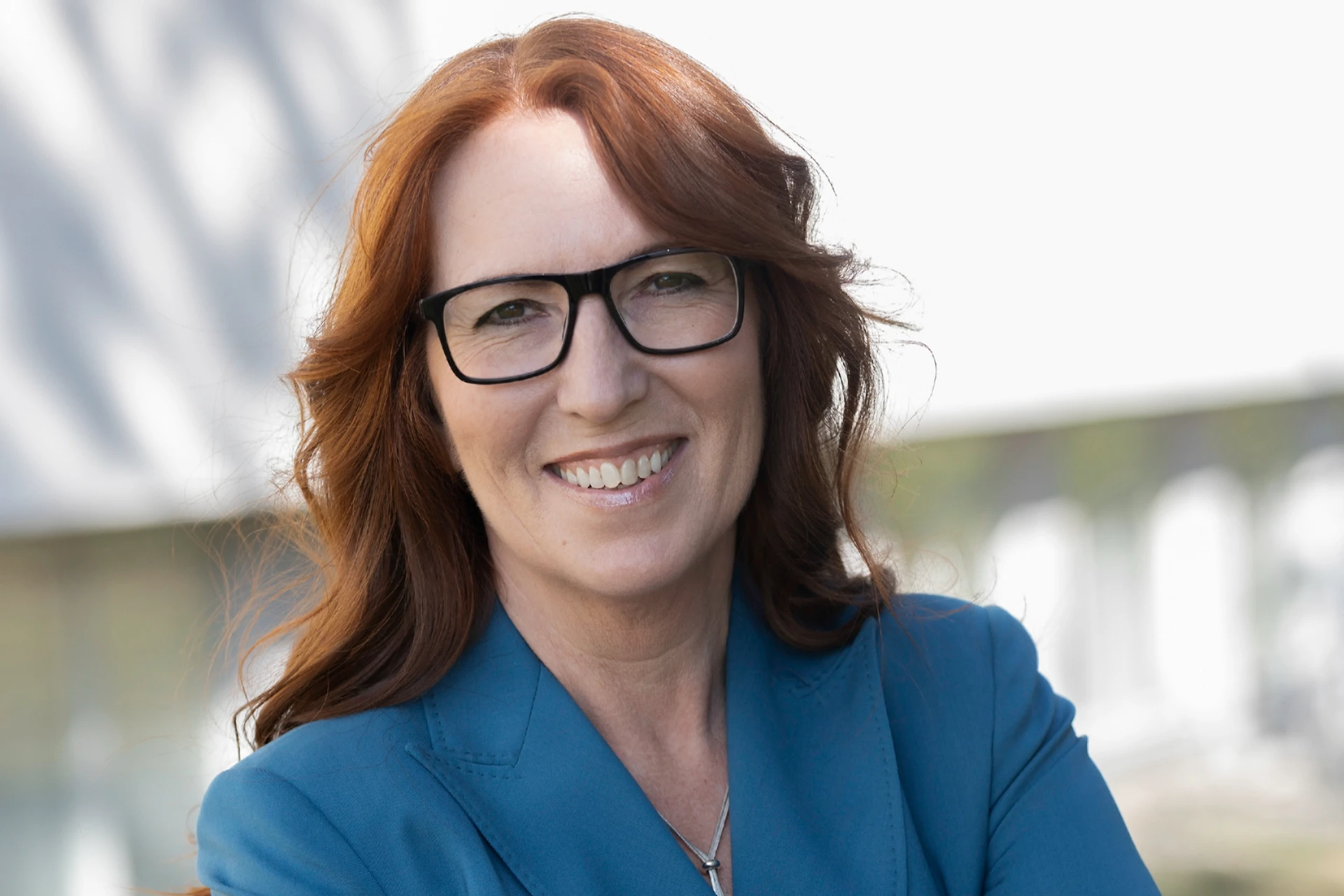 Författaren Helén Rigamonti, expert inom Customer Experience, ler mot kameran i varm blå/turkos kavaj framför en vit fasad.