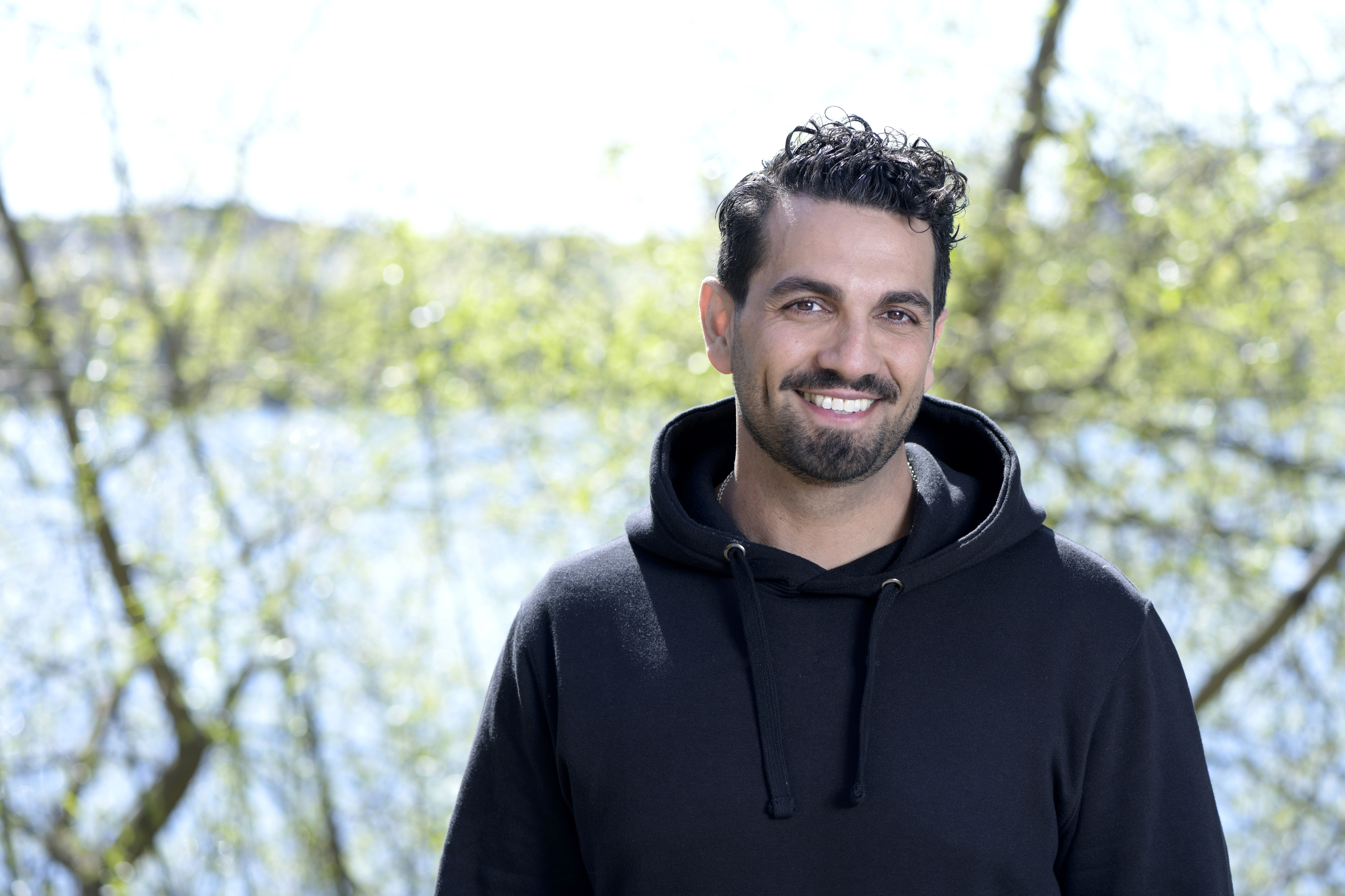 Bilden visar författaren och fd polisen Nadim Ghazale, leende med en sjö och träd i bakgrunden. 