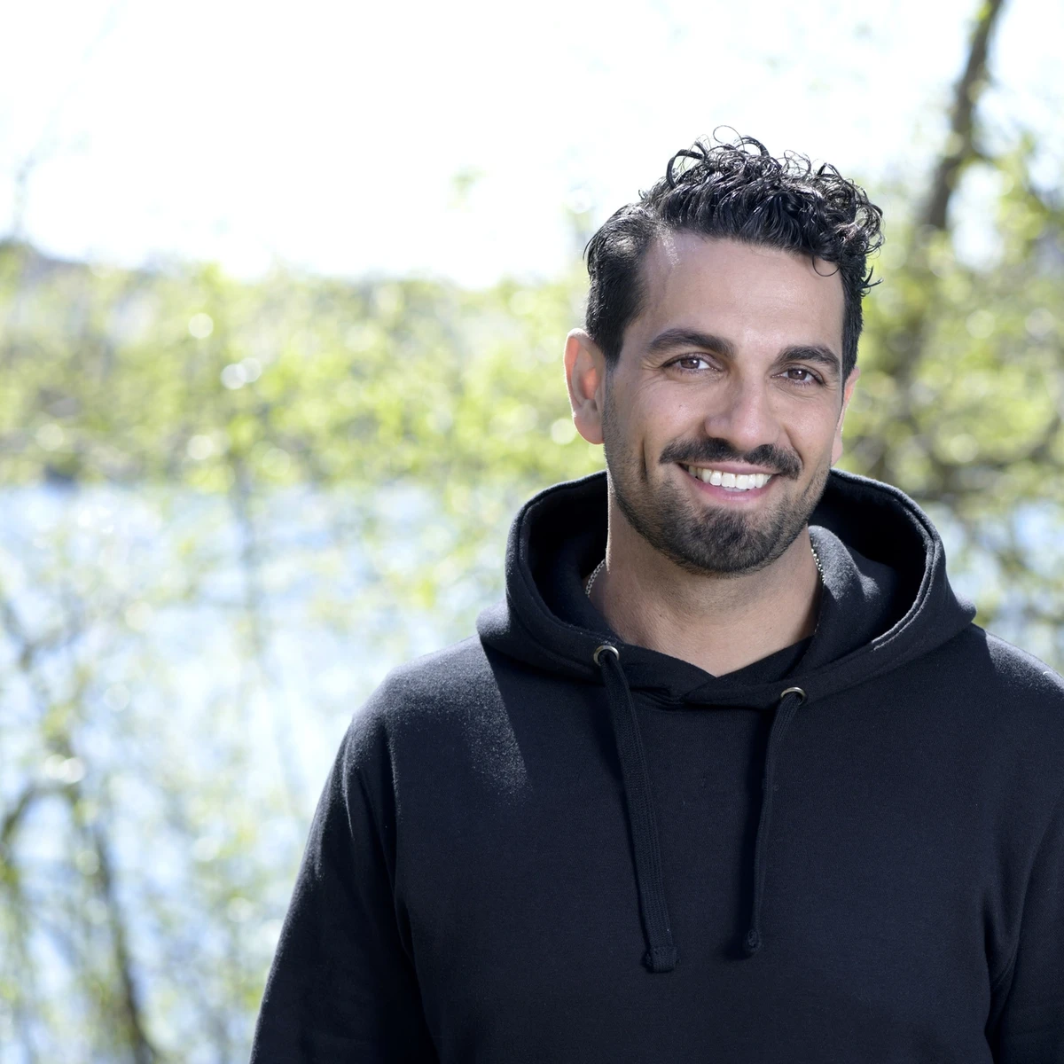 BYWRTRS leende Nadim Ghazale, polis och föreläsare, i svart hoodie med natur som bakgrund