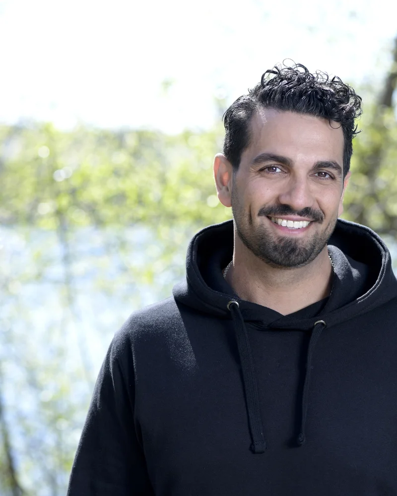 Bilden visar författaren och fd polisen Nadim Ghazale, leende med en sjö och träd i bakgrunden.