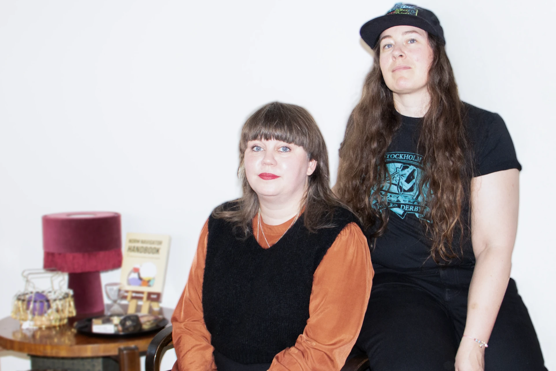 Pernilla Alexandersson sitter framför Jenny Claesson bredvid ett litet bord med en lampa på.