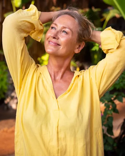 Hälsoguru & Författare Karin Björkegren i gul härlig blus med armarna uppåt tittandes mot solen. Natur i bakgrunden.