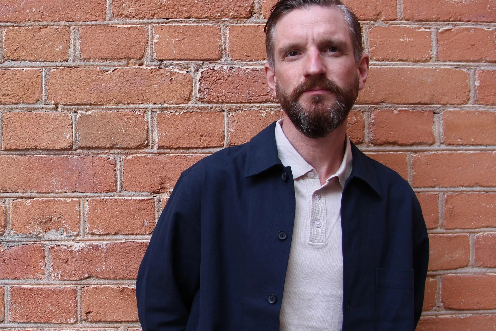 Författaren och föreläsaren Klas Fjärstedt står framför en tegelvägg. Han har en vit pikétröja under en mörkblå skjortjacka.