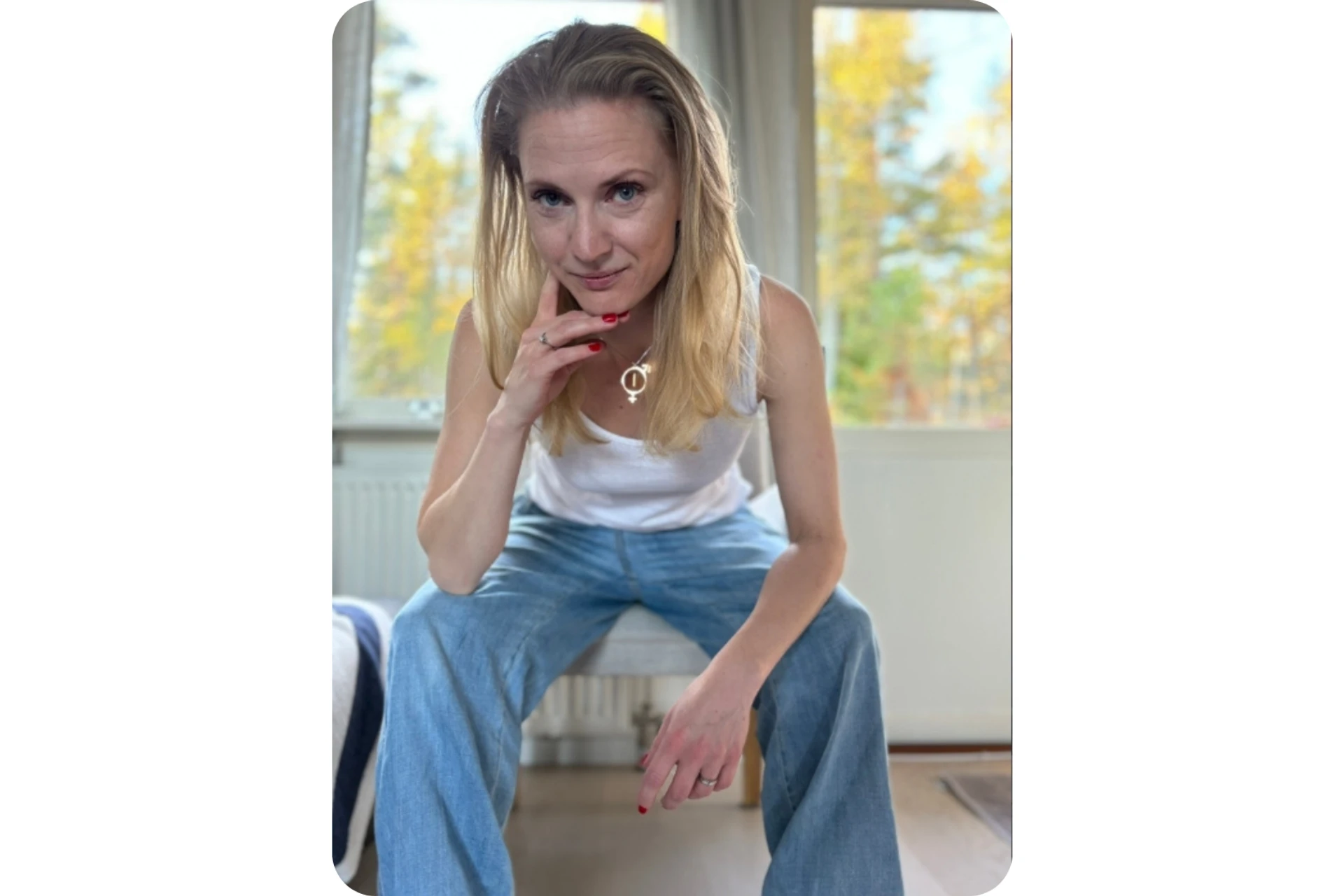 Elisabeth Wadin sitter framåtlutad på en stol i jeans och vitt linne, med fönster i bakgrunden.