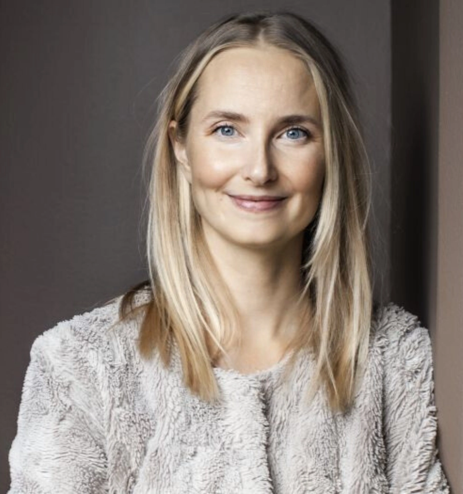 Bilden visar psykologen Katarina Blom i en grå, mjuk kofta, lutad mot en vägg. 