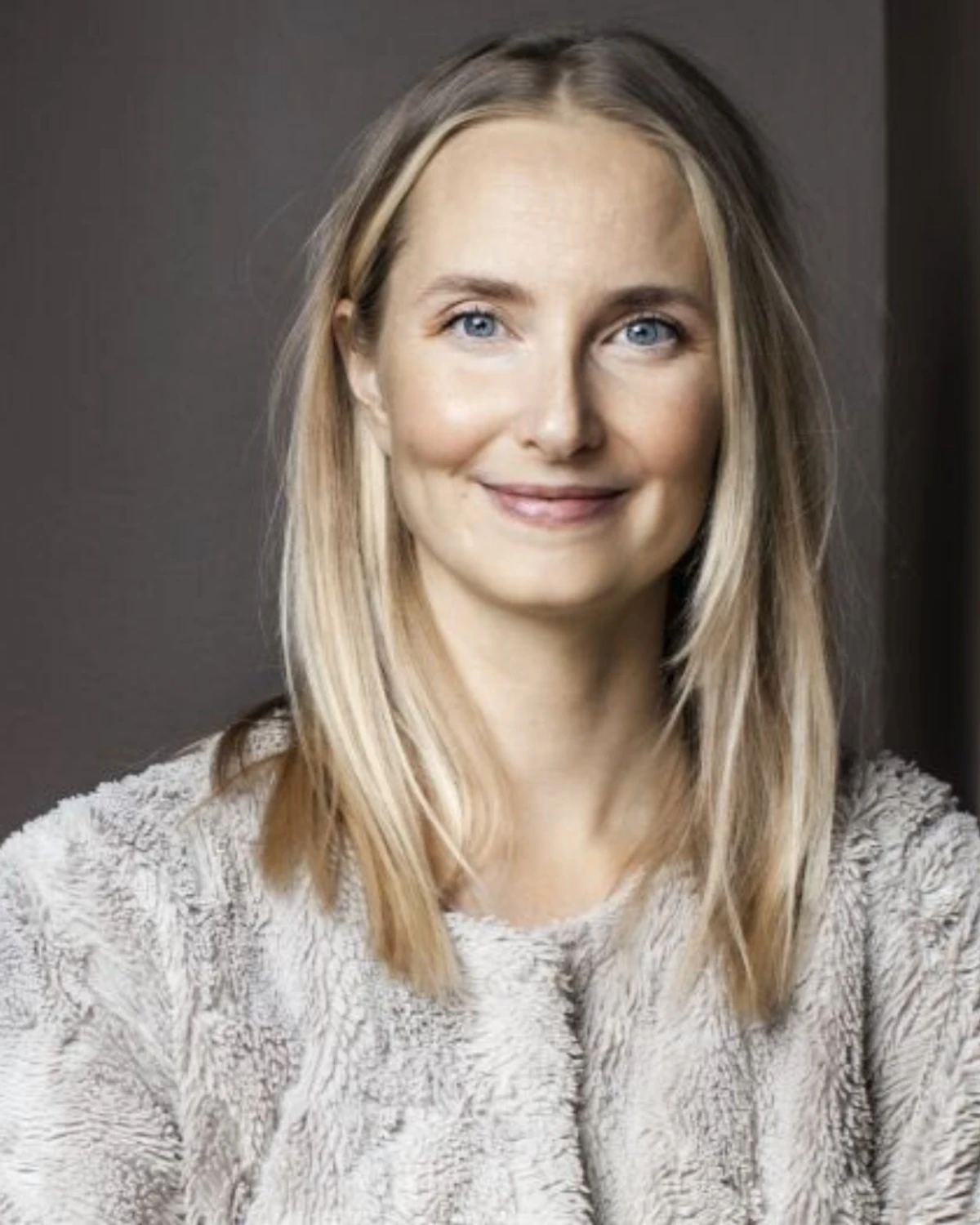 Bilden visar psykologen Katarina Blom i en grå, mjuk kofta, lutad mot en vägg.