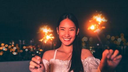 Smiling woman in white top holding sparklers to celebrate New Year’s Day.