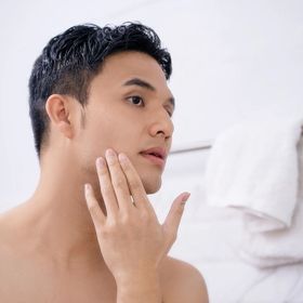 Young Asian male puts his hand near jawline to check his skin.