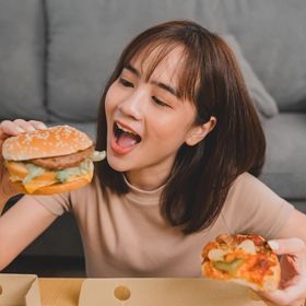 A woman eating a burger and a slice of pizza.