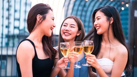 Three smiling women toasting their glasses while at a party.